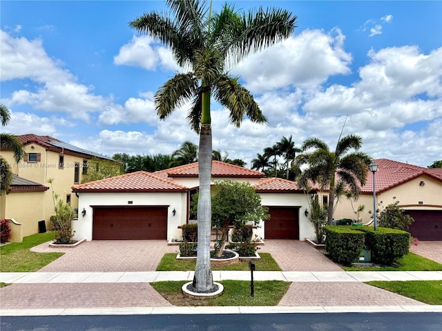 mediterranean / spanish house with a garage, a tile roof, stucco siding, and decorative driveway