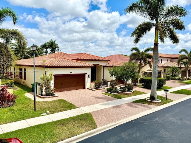 mediterranean / spanish home with a tile roof, decorative driveway, a front lawn, an attached garage, and stucco siding