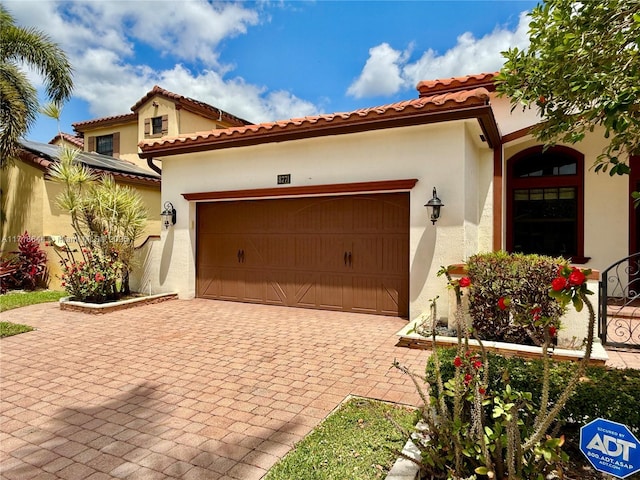 exterior space with an attached garage, a tile roof, decorative driveway, and stucco siding