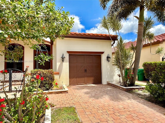 mediterranean / spanish-style house featuring stucco siding, decorative driveway, a tiled roof, and a garage