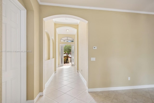 corridor featuring baseboards, arched walkways, crown molding, and light tile patterned floors