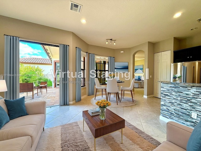 living area with arched walkways, visible vents, a textured ceiling, and light tile patterned floors