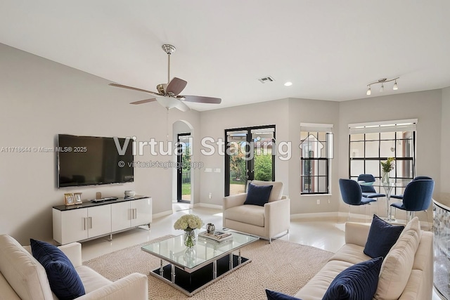 living area with arched walkways, visible vents, baseboards, and ceiling fan