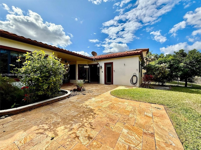 back of property with fence, a tile roof, stucco siding, a lawn, and a patio