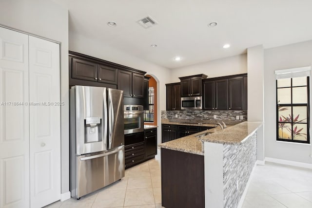 kitchen featuring light tile patterned floors, arched walkways, light stone countertops, decorative backsplash, and appliances with stainless steel finishes