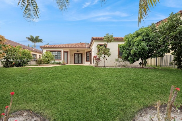 mediterranean / spanish-style house with stucco siding, a tile roof, fence, french doors, and a front yard