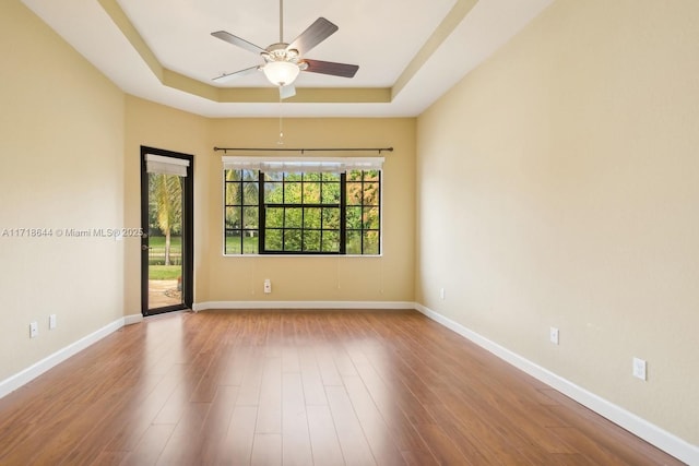 spare room with ceiling fan, baseboards, a tray ceiling, and wood finished floors