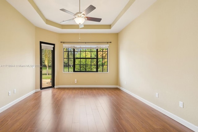 empty room featuring a tray ceiling, wood finished floors, a ceiling fan, and baseboards
