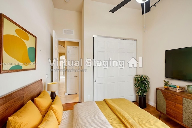 bedroom with visible vents, a ceiling fan, wood finished floors, a high ceiling, and a closet