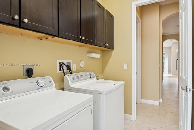 laundry room featuring baseboards, washing machine and clothes dryer, light tile patterned flooring, cabinet space, and arched walkways