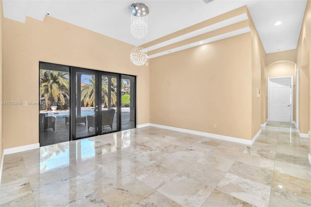 unfurnished room featuring a high ceiling, a notable chandelier, and french doors