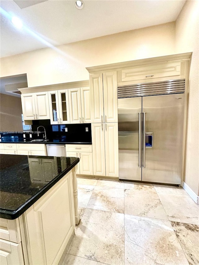 kitchen with stainless steel appliances, dark stone countertops, cream cabinetry, and tasteful backsplash