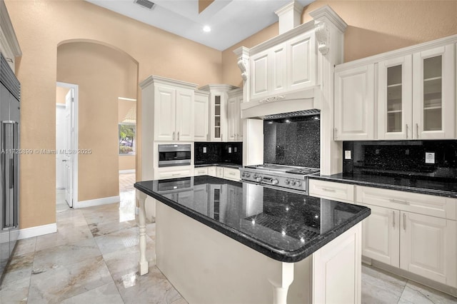 kitchen featuring dark stone countertops, stainless steel appliances, white cabinets, a kitchen island, and decorative backsplash