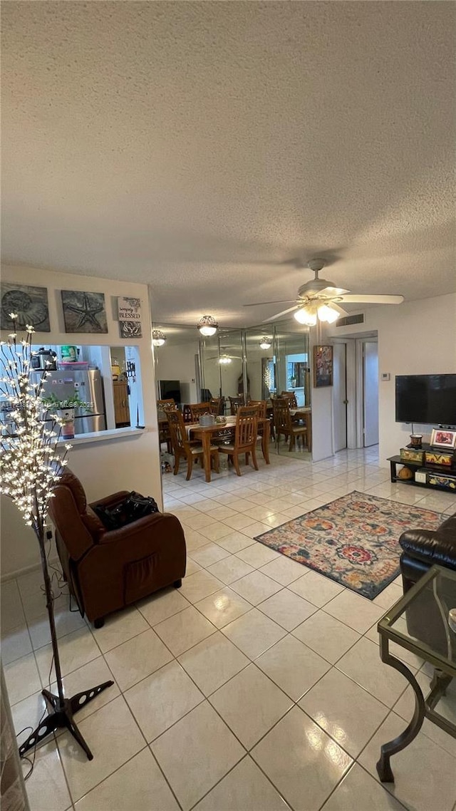 living room with a textured ceiling, ceiling fan, and light tile patterned floors