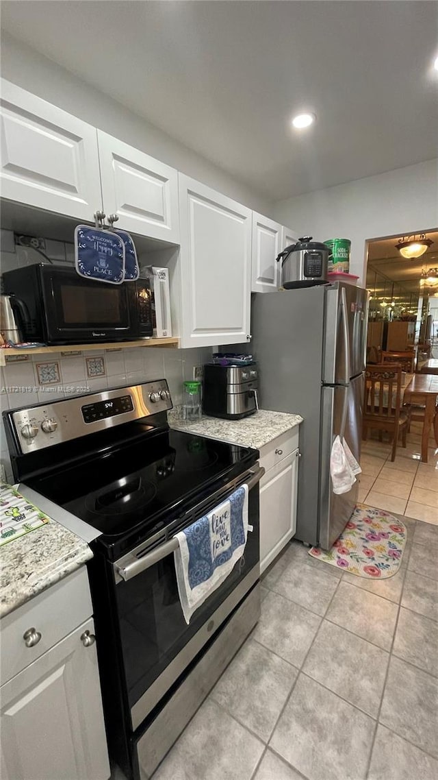 kitchen with light stone counters, stainless steel appliances, light tile patterned floors, and white cabinetry