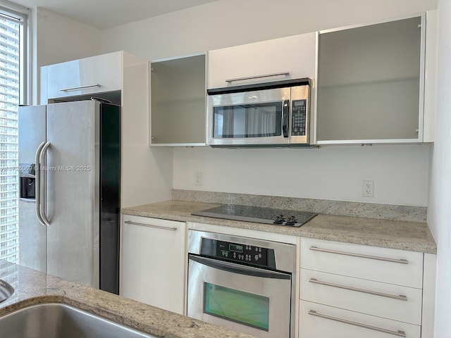 kitchen featuring stainless steel appliances, white cabinetry, and light stone countertops