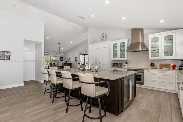 kitchen with white cabinetry, a center island with sink, wall chimney exhaust hood, and a kitchen bar