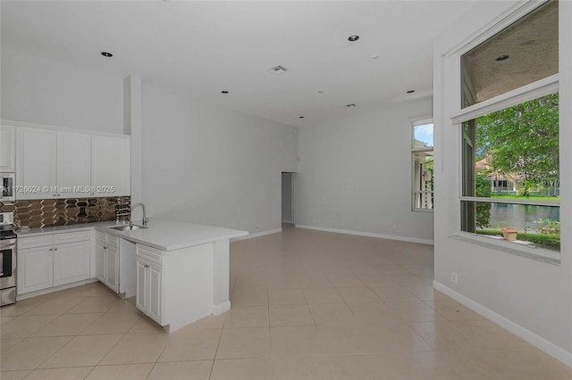 kitchen featuring kitchen peninsula, light tile patterned flooring, a water view, white cabinets, and sink