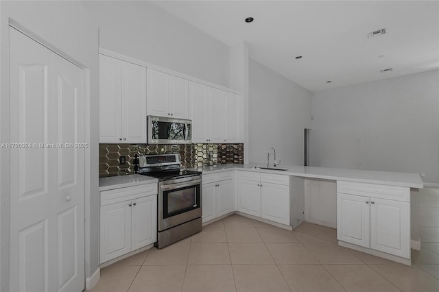 kitchen featuring light tile patterned floors, white cabinetry, kitchen peninsula, appliances with stainless steel finishes, and sink