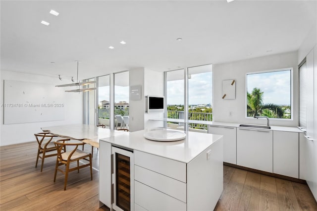 kitchen with light hardwood / wood-style flooring, a wealth of natural light, a center island, wine cooler, and white cabinets