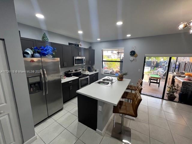 kitchen with an island with sink, a breakfast bar area, appliances with stainless steel finishes, light tile patterned flooring, and sink