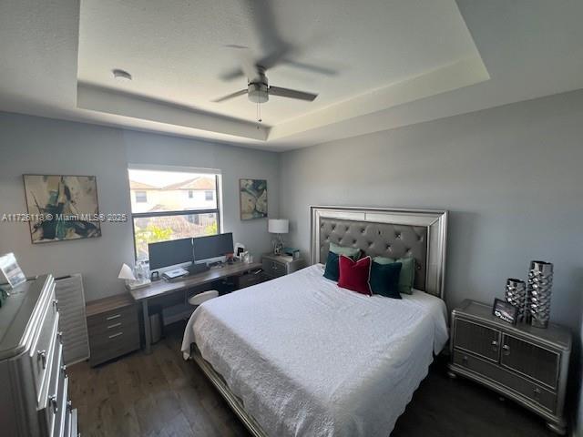 bedroom with dark wood-type flooring, a raised ceiling, and ceiling fan