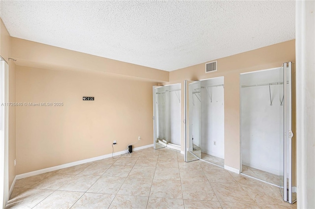 unfurnished bedroom with a textured ceiling, multiple closets, and light tile patterned flooring