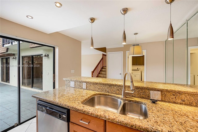 kitchen featuring decorative light fixtures, stainless steel dishwasher, sink, washer and clothes dryer, and light stone countertops