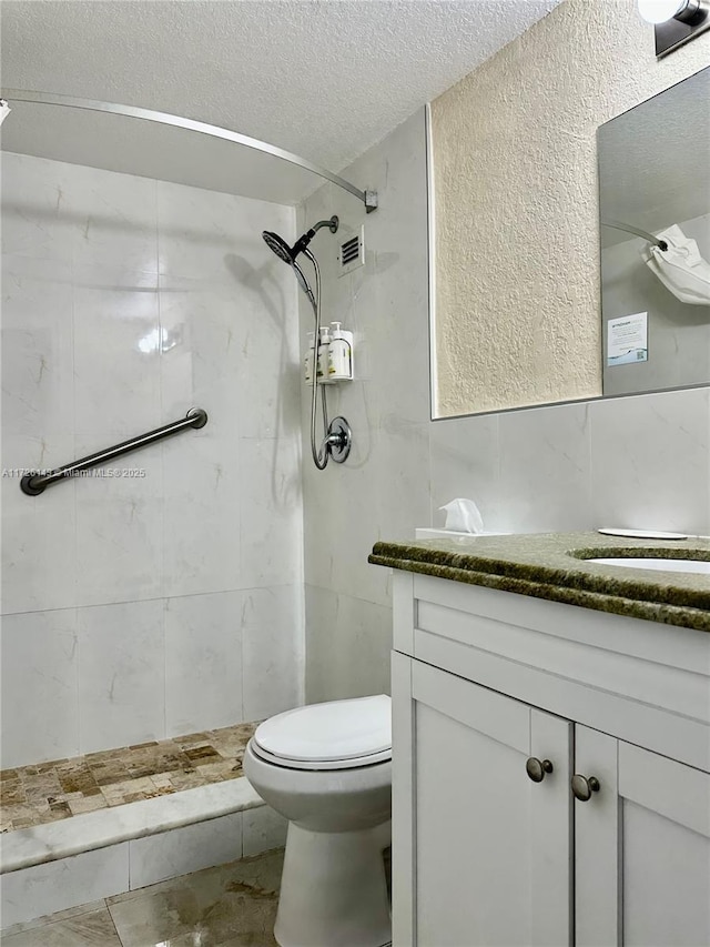 bathroom featuring toilet, vanity, tile walls, tiled shower, and a textured ceiling