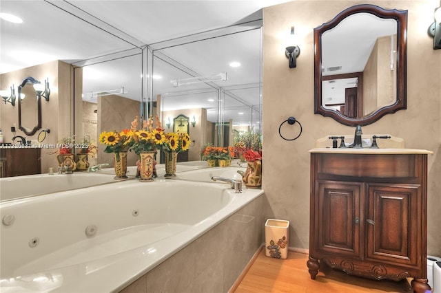 bathroom with wood-type flooring, vanity, and a relaxing tiled tub