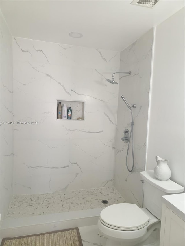 bathroom with a tile shower, vanity, and toilet