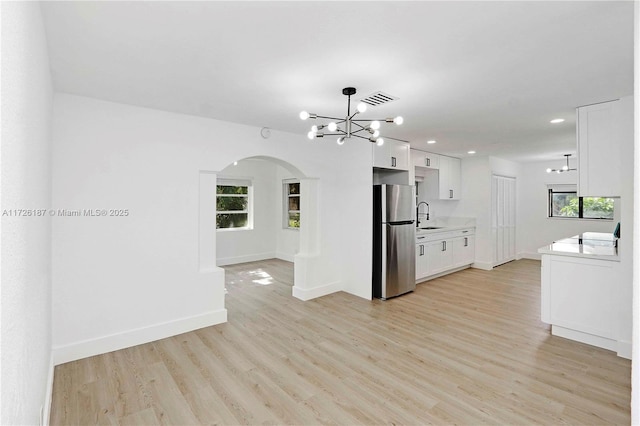 kitchen featuring sink, white cabinets, light hardwood / wood-style floors, stainless steel refrigerator, and hanging light fixtures