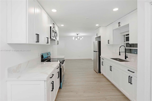 kitchen with appliances with stainless steel finishes, light hardwood / wood-style floors, light stone counters, white cabinets, and sink