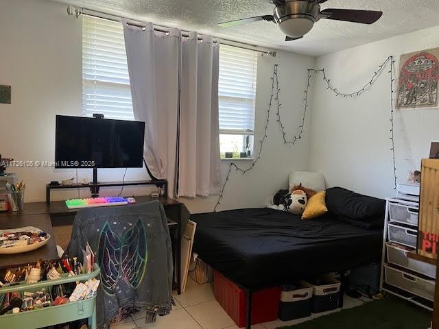 tiled bedroom with ceiling fan and a textured ceiling