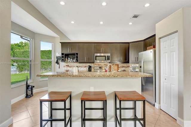 kitchen with appliances with stainless steel finishes, a kitchen island with sink, decorative backsplash, and dark brown cabinetry