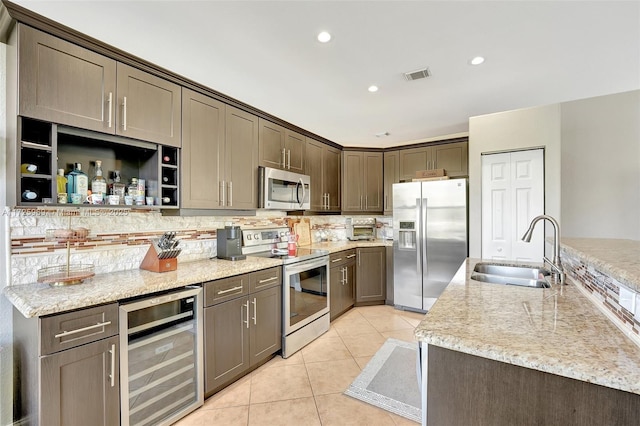 kitchen with light stone counters, stainless steel appliances, light tile patterned floors, beverage cooler, and sink