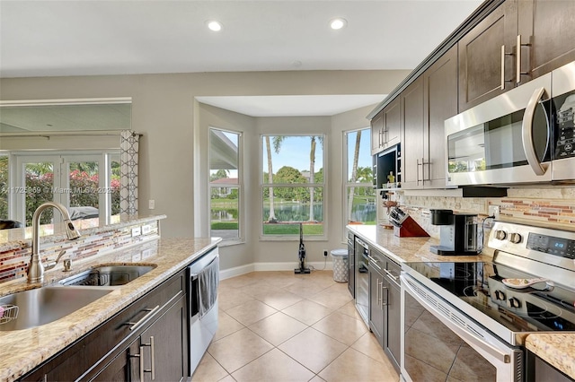 kitchen with light stone countertops, sink, backsplash, appliances with stainless steel finishes, and dark brown cabinetry