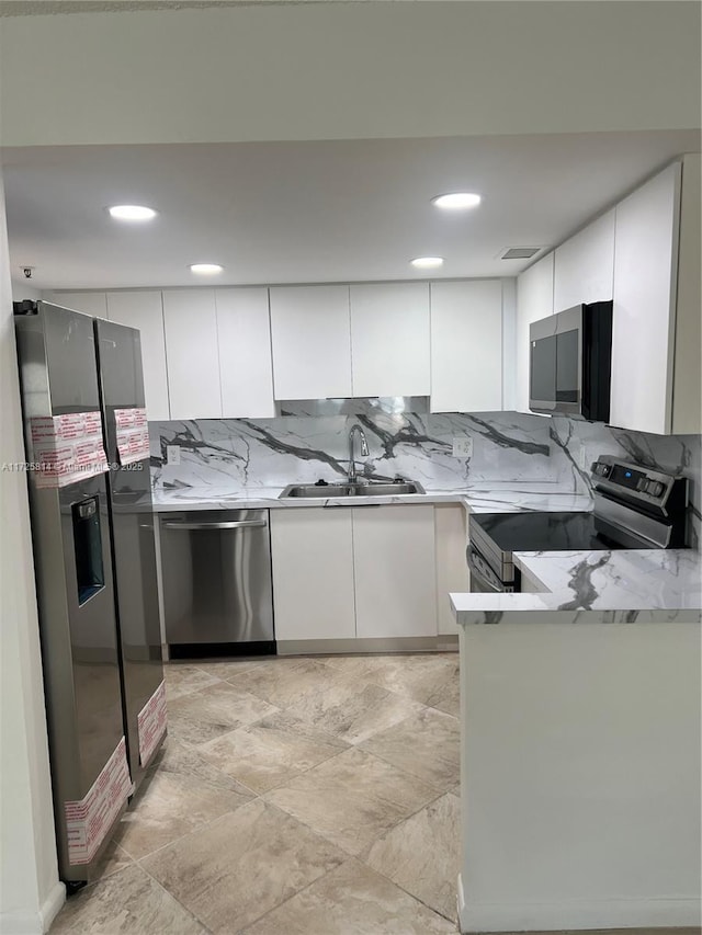 kitchen featuring stainless steel appliances, a sink, white cabinetry, light countertops, and decorative backsplash