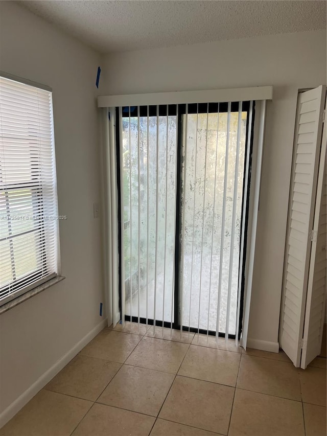 empty room with light tile patterned floors, a textured ceiling, and baseboards