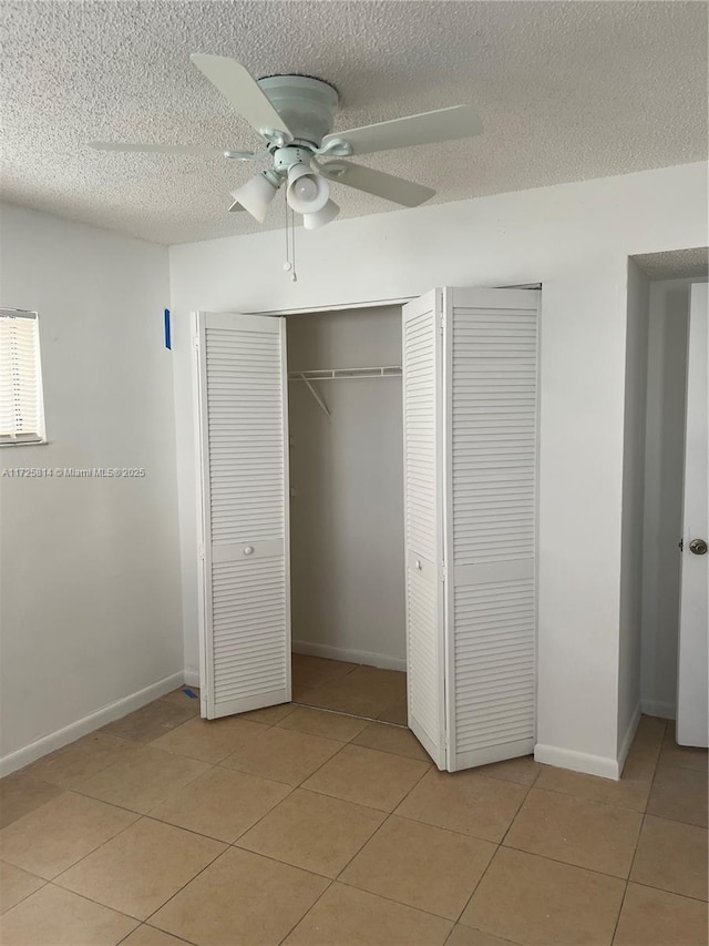 unfurnished bedroom featuring a textured ceiling, a closet, light tile patterned flooring, and baseboards