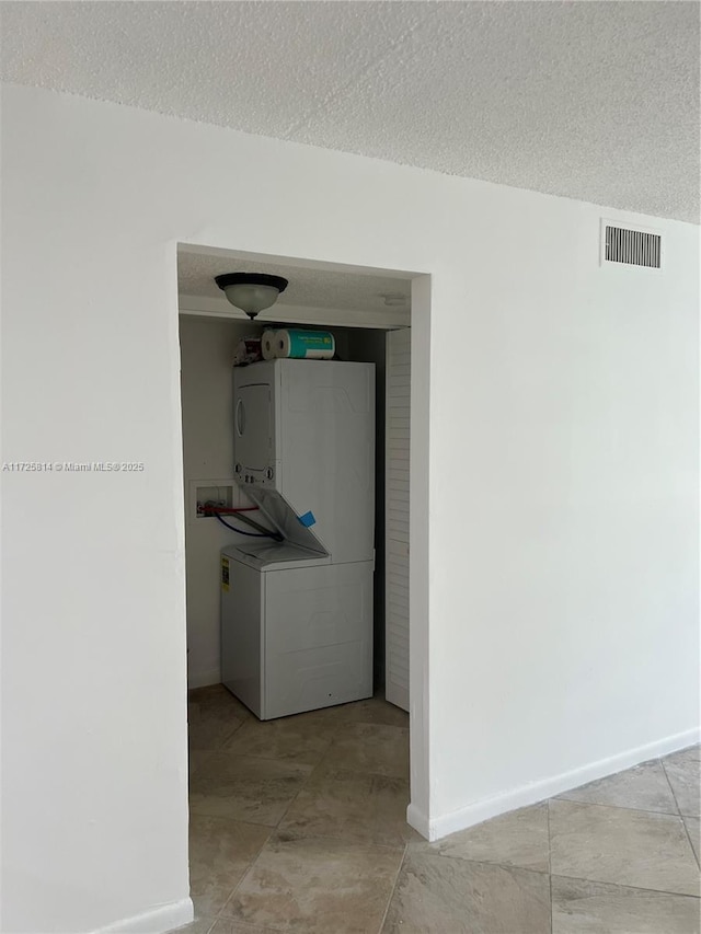 corridor with baseboards, visible vents, a textured ceiling, and stacked washer and clothes dryer