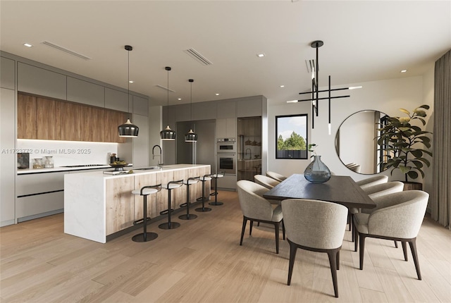 dining space with an inviting chandelier, light hardwood / wood-style floors, and sink