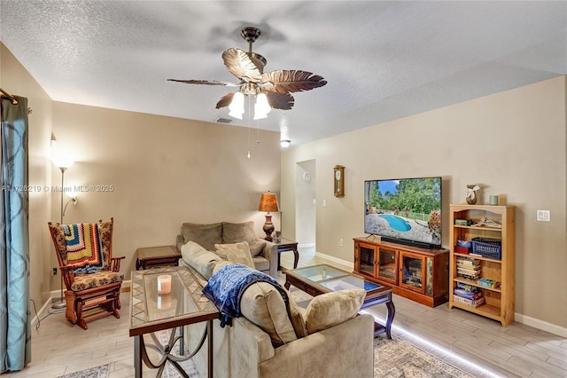 living room with a textured ceiling, ceiling fan, and light hardwood / wood-style flooring