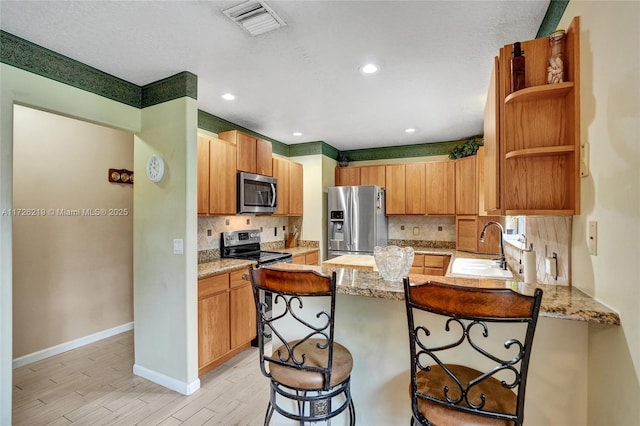 kitchen with sink, a kitchen breakfast bar, light hardwood / wood-style floors, light stone countertops, and appliances with stainless steel finishes