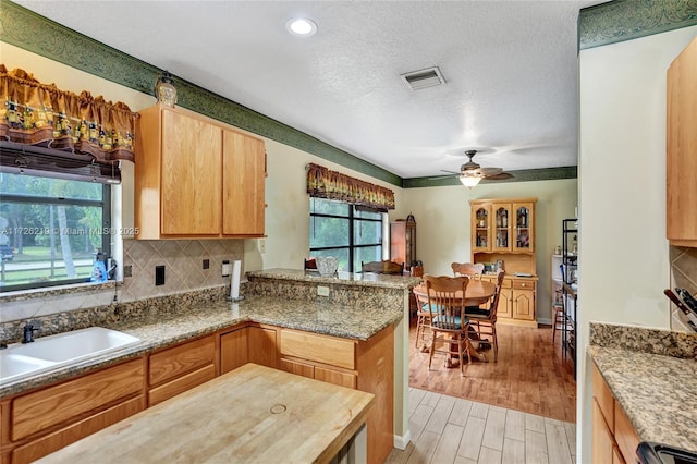 kitchen featuring kitchen peninsula, ceiling fan, a textured ceiling, light stone counters, and sink