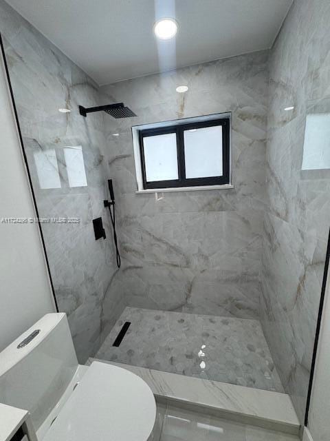 bathroom with a tile shower, vanity, and toilet