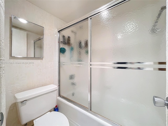 bathroom featuring toilet and shower / bath combination with glass door