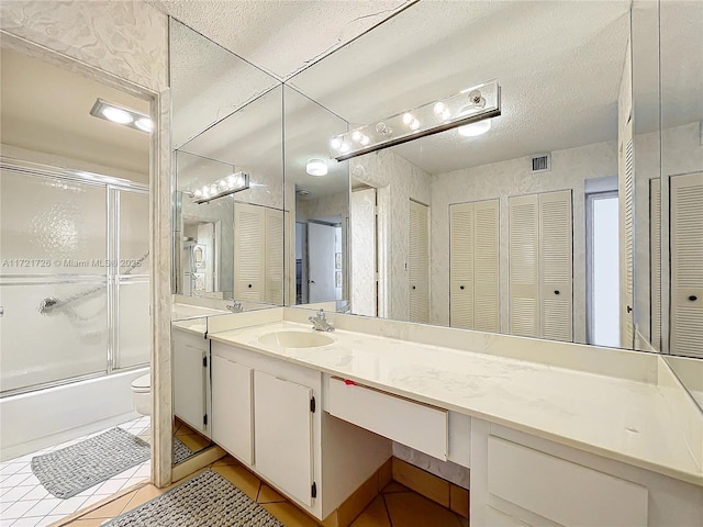 full bathroom with combined bath / shower with glass door, vanity, tile patterned floors, and toilet