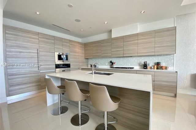 kitchen featuring an island with sink, light tile patterned floors, oven, a breakfast bar area, and sink