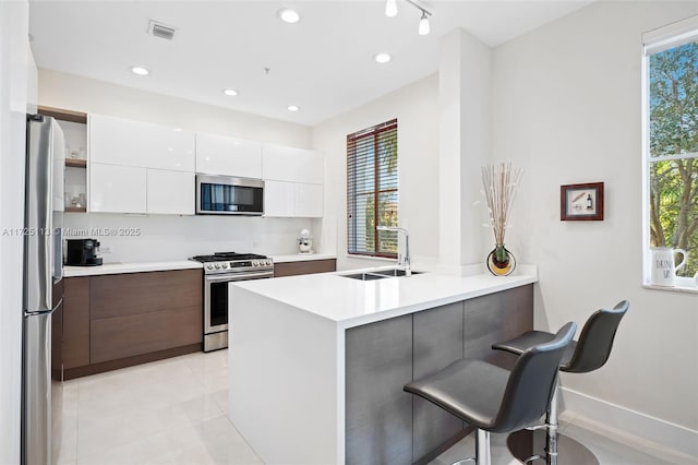 kitchen featuring a kitchen bar, kitchen peninsula, appliances with stainless steel finishes, white cabinets, and sink